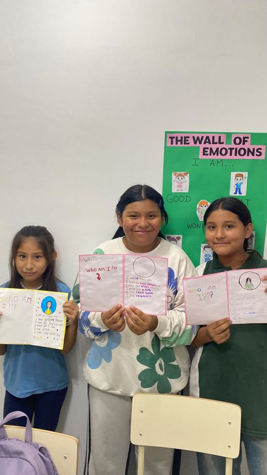 Tres estudiantes muestran sus cuadernillos frente al mural The Wall of Emotions