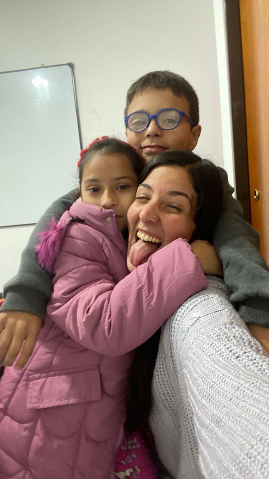Docente abrazando a dos estudiantes en el aula de Lingos Escobar