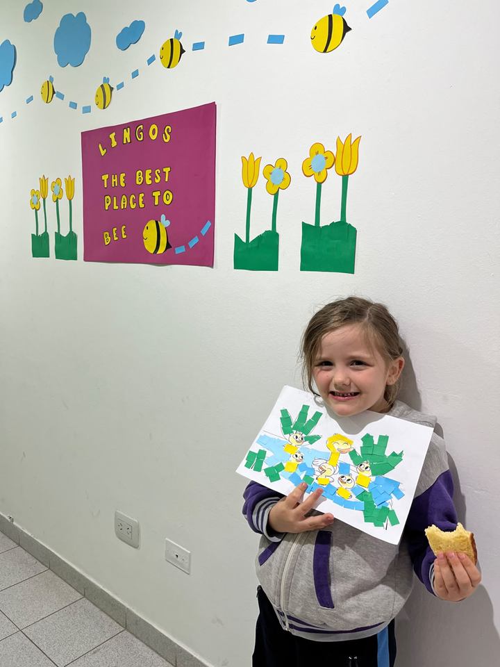Estudiante muestra una flor de papel frente a la pared de abejas del aula